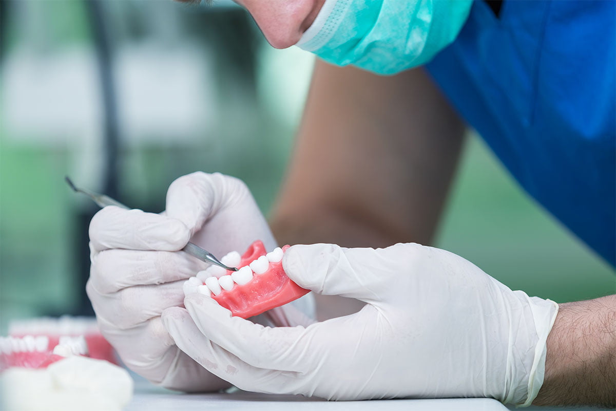 Dental prosthesis, dentures, prosthetics work. Prosthetics hands while working on the denture, false teeth, a study and a table with dental tools.